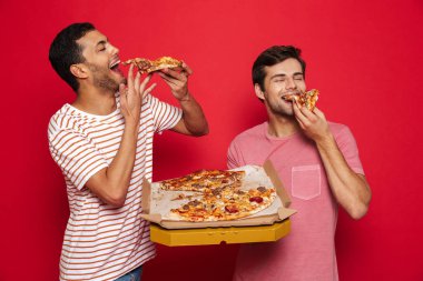 Yakışıklı bir görüntüsünü mutlu büyük pizza yemek tutan kırmızı duvar arka plan üzerinde genç erkek arkadaş izole memnun.