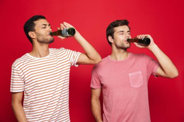 Şişe soda su içme izole kırmızı arka plan üzerinde duran iki neşeli genç adam