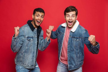İki kırmızı arka plan üzerinde izole ayakta kot ceketler giyen genç erkek arkadaş heyecanlı kutluyor