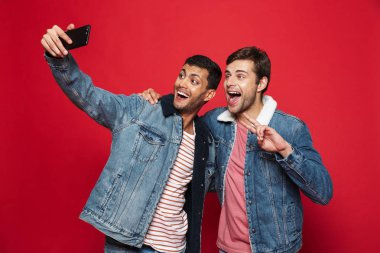 Bir selfie alarak izole kırmızı arka plan üzerinde duran iki neşeli genç adam