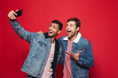 Bir selfie alarak izole kırmızı arka plan üzerinde duran iki neşeli genç adam