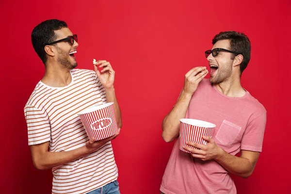 Twee Vrolijke Jonge Mannen Permanent Geïsoleerd Rode Achtergrond Eten Van — Stockfoto