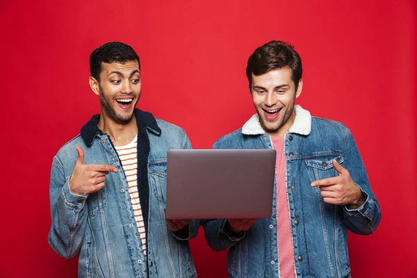 Два Веселых Молодых Человека Стоящих Изолированно Красном Фоне Держа Ноутбук — стоковое фото