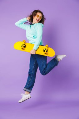 Görüntü şaşırtıcı bir mutlu genç kadının poz kaykay tutan mor arka plan duvardan izole.