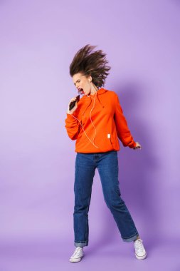 Genç kadının müzik dinleme mor arka plan duvar telefon şarkı tutan earphones ile izole görüntü.