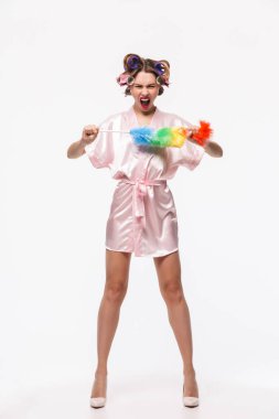 Saçında beyaz arka plan üzerinde izole ayakta bornoz giymiş curlers ile oldukça sinirli bir ev hanımı bir silgi ile poz tam uzunlukta portresi