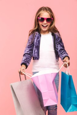 Alışveriş çantaları taşırken pembe arka plan üzerinde izole neşeli küçük kız