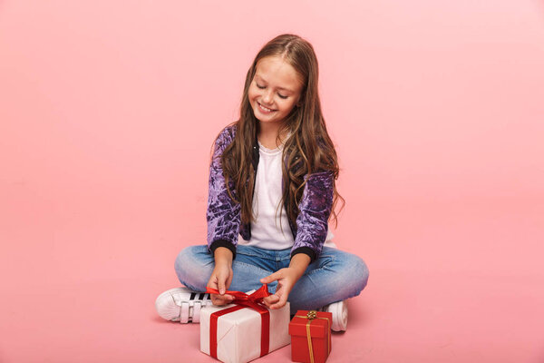 Возбужденная маленькая девочка сидит изолированный на розовом фоне, выбирая между малыми и большими подарочными коробками
