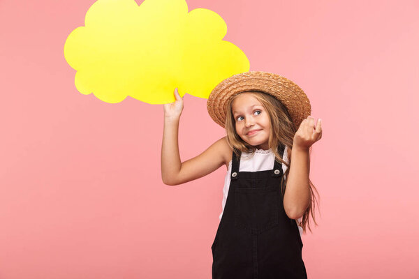 Portrait of a cheerful little girl wearing summer hat isolated over pink background, holding empty speech bubble