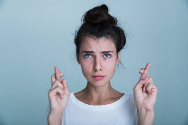 Mavi arka plan üzerinde izole rahat güzel bir genç kız portresi, parmak tutan şans getirmesi için çarpı işareti