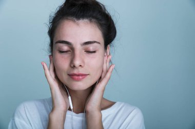 Kulaklık ile müzik dinlemek üzerinde mavi arka plan, izole bir güzel genç casual kız ayakta, yakın çekim