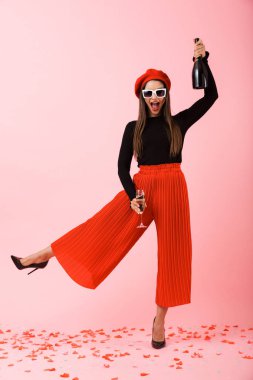 Güneş gözlüğü ve kutlama, holding, şampanya ve bir bardak kırmızı bere giyen neşeli genç kadın