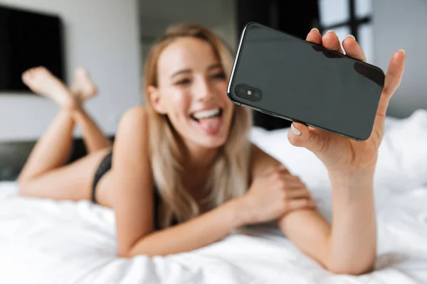 Красивая молодая женщина в нижнем белье утром в постели дома сделать селфи по мобильному телефону . — стоковое фото