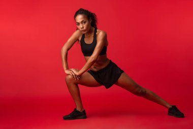 Görüntü izole kırmızı duvar arka plan üzerinde bir güçlü genç Afrika spor fitness kadının poz yapmak egzersizleri.