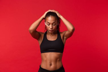 Görüntü izole kulaklık ile müzik dinleme kırmızı duvar arka plan üzerinde bir güzel genç Afrika spor fitness kadının poz.