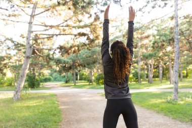 Image of skinny woman 20s wearing black tracksuit working out and stretching body in green park clipart