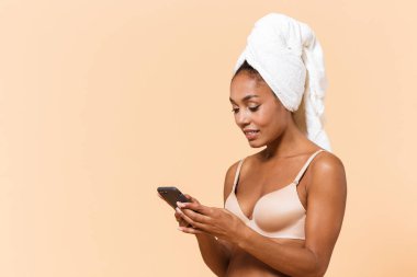 Havlu ve cep telefonu bej renkli arka plan üzerinde izole kullanarak giyen beyaz iç çamaşırı sarılı esmer kadın portresi