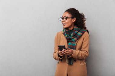 Afrikalı kadın giyiyor kat ayakta cep telefonu üzerinde konuşurken gri arka plan üzerinde gülümseyen