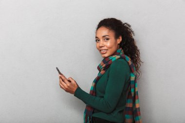 Afrikalı kadın giyiyor kat ayakta cep telefonuyla gri arka plan üzerinde gülümseyen