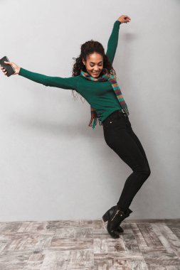 Cep telefonu tutan gri arka plan üzerinde atlama şal çok Afrika bir kadının tam uzunlukta portarit