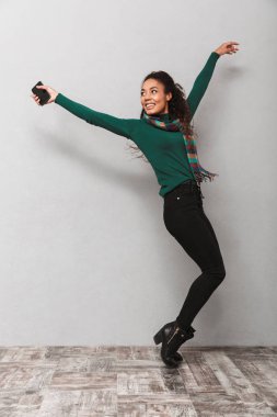 Cep telefonu tutan gri arka plan üzerinde atlama şal çok Afrika bir kadının tam uzunlukta portarit