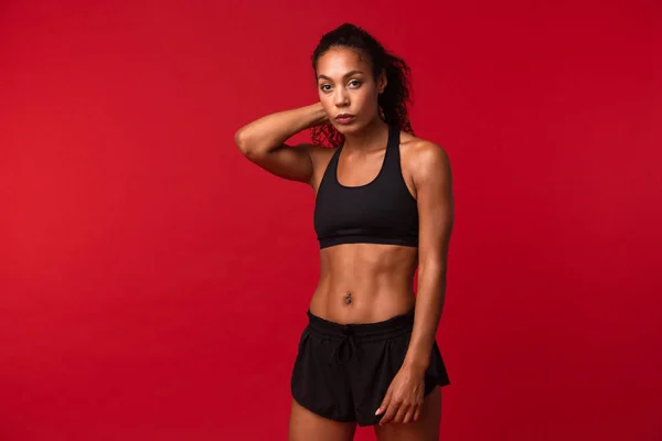 Portrait of well-built african american woman in black sportswear standing isolated over red background