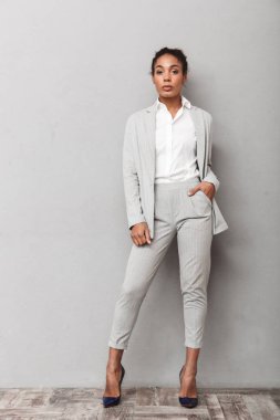 Gri arka plan üzerinde duran, poz takım elbise giymiş bir emin Afrika iş kadını tam uzunlukta portresi