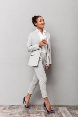 Paket servisi olan restoran kahve tutan takım ayakta gri arka plan üzerinde giyen bir emin Afrika iş kadın portresi tam uzunlukta