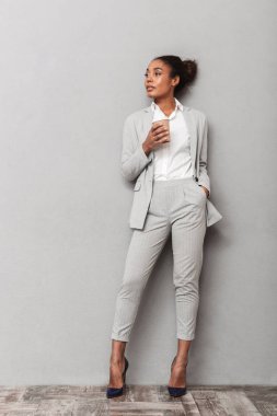 Paket servisi olan restoran kahve tutan takım ayakta gri arka plan üzerinde giyen bir emin Afrika iş kadın portresi tam uzunlukta