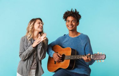 Mutlu genç multiethninc çift birlikte, üzerinde mavi arka plan izole bir gitar çalmak