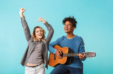 Mutlu genç multiethninc çift birlikte, üzerinde mavi arka plan izole bir gitar çalmak