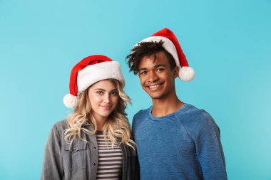 Mutlu çok ırklı genç çift üzerinde mavi arka plan izole Noel kırmızı şapka