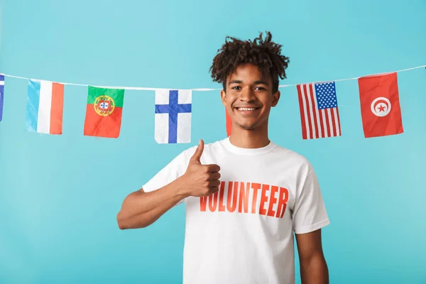 一个面带微笑的非洲年轻人的肖像 穿着华丽的 T恤站在蓝色背景孤立 显示竖起大拇指 — 图库照片
