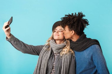 Mutlu genç çift izole mavi arka plan üzerinde duran, bir selfie alarak, Öpüşme