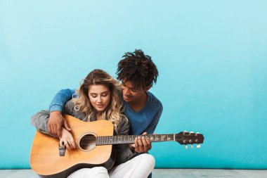 Mutlu genç multiethninc çift birlikte, üzerinde mavi arka plan izole bir gitar çalmak