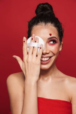 Toz puf tutan makyaj ayakta poz, kırmızı arka plan üzerinde izole giyen bir çekici genç üstsüz kadın güzellik portresi