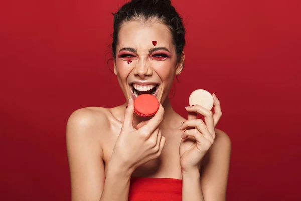 一个有吸引力的年轻赤裸上身的女人化妆的美丽肖像站在孤立的红色背景 吃马卡龙 — 图库照片