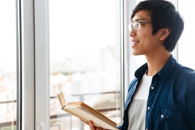Gülümseyen Asya adam evde pencereden duran bir kitap okuma