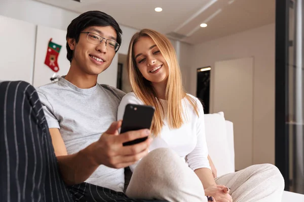 快乐的年轻夫妇坐在家里的沙发上 看着手机 — 图库照片