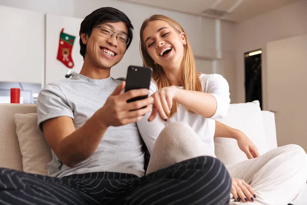 Alegre Pareja Joven Sentados Juntos Sofá Casa Mirando Teléfono Móvil —  Fotos de Stock