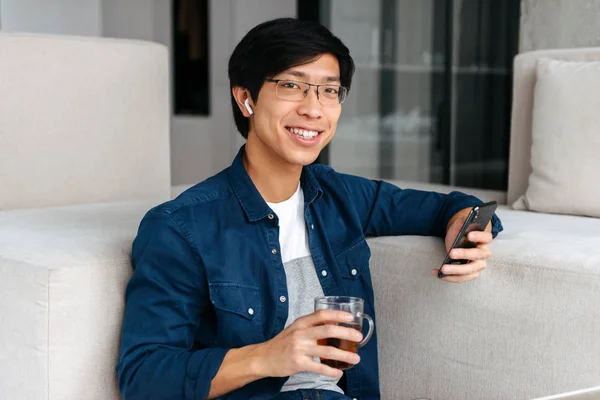 Feliz Asiático Homem Sentado Sofá Casa Usando Fones Ouvido Usando — Fotografia de Stock