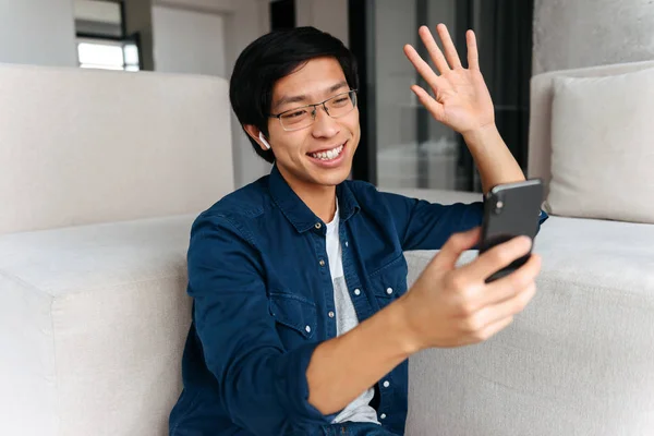 Feliz Asiático Homem Sentado Sofá Casa Usando Fones Ouvido Usando — Fotografia de Stock