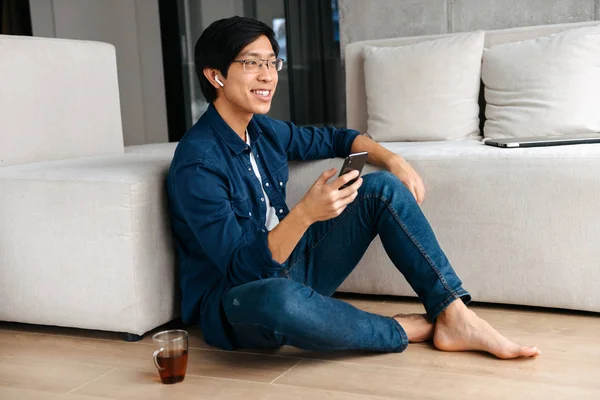 Happy Asijské Muž Sedí Gauči Doma Nosit Sluchátka Pomocí Mobilního — Stock fotografie