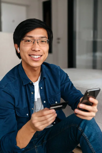 Happy Asian Man Sitting Couch Home Wearing Earphones Using Mobile — Stock Photo, Image