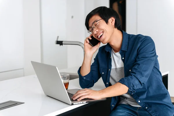 Mosolyogva Ázsiai Ember Dolgozik Laptop Számítógép Otthon Beszél Mozgatható Telefon — Stock Fotó