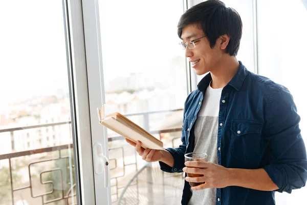 Leende Asiatisk Man Bok När Står Vid Fönstret Hemma — Stockfoto