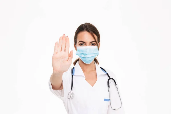自信的年轻女医生穿着制服站在白色背景隔离 显示停止手势 — 图库照片