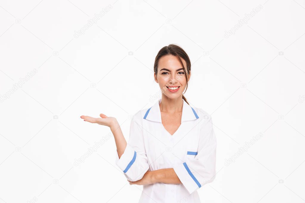 Beautiful young woman doctor wearing uniform standing isolated over white background, presenting copy space