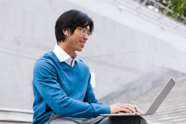 Açık havada dizüstü bilgisayar kullanan gülümseyen Asya iş adamı