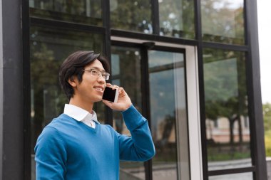 Açık havada yürürken cep telefonu üzerinde konuşurken gülümseyen genç Asya iş adamı